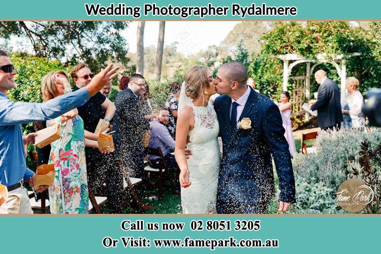 Photo of the Bride and the Groom kissing while showering rice by the visitors Rydalmere NSW 2116