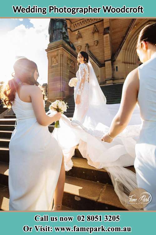 Photo of the Bride smiling on the bridesmaid holding the tail of her wedding gown at the front of the church Woodcroft NSW 2767